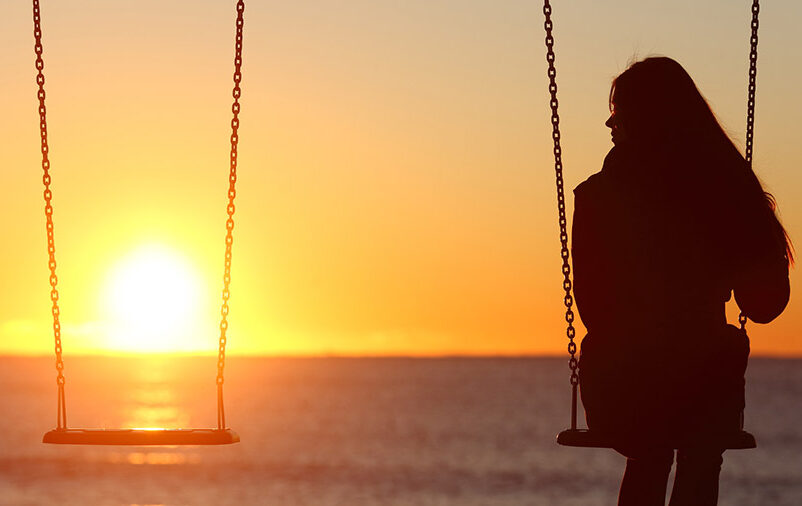 Mulher sozinha no balanço ao pôr do sol